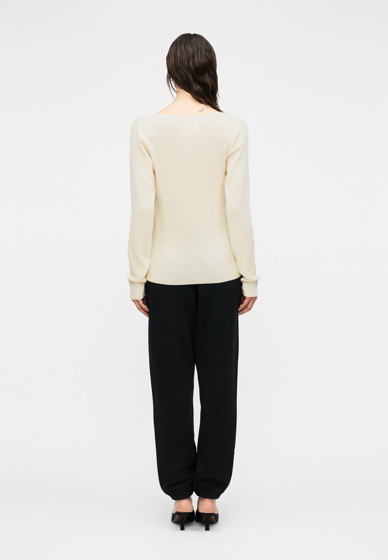 Pull en maille de couleur crème avec un large décolleté, associé à un pantalon de survêtement noir ample et des chaussures noires à talons.