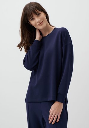 Navy blue long-sleeve top in soft material, relaxed fit, round neckline, side slit hem, featuring dropped shoulders and subtle texture.