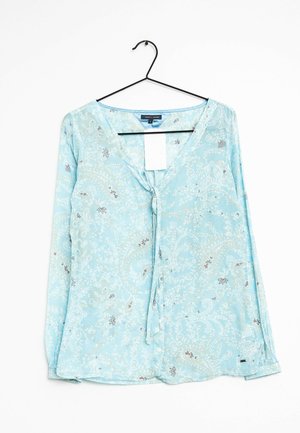 Himmelbluse mit langen Ärmeln und einer Schleife vorne, die ein Paisleymuster in verschiedenen Farben und einen subtilen Glanz aufweist. Anhänger angebracht.