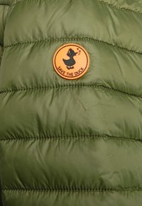 Zielona puchowa kurtka o błyszczącej fakturze, z poziomymi przeszyciami i pomarańczową okrągłą łatą z wizerunkiem kaczki oraz napisem "URATUJ KACZKĘ".