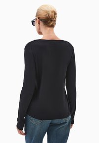 Czarny top z długimi rękawami i okrągłym dekoltem, gładka tekstura i dopasowany krój, w połączeniu z niebieskimi dżinsami. Prosty, minimalistyczny design.