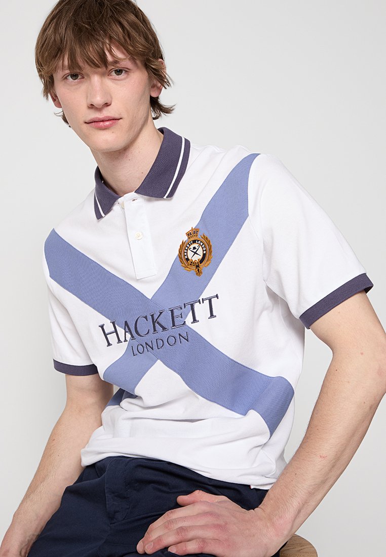 Polo shirt blanc avec des rayures diagonales bleues, col sombre et logo brodé "Hackett London" sur la poitrine. Manches courtes avec des accents.