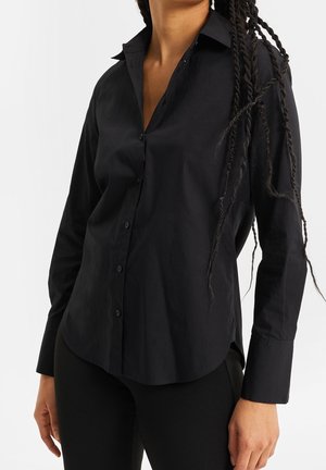 Czarna koszula na guziki wykonana z gładkiej tkaniny, z klasycznym kołnierzykiem, długimi rękawami i zaokrąglonym dołem. Bez widocznych wzorów ani ozdób.