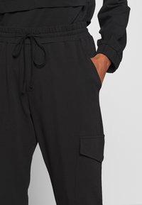 Czarne dresowe spodnie uszyte z miękkiego materiału, z elastycznym pasem w talii z troczkiem, boczną kieszenią oraz kieszenią na udzie.