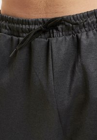 Mørk grå joggebukser med elastisk midjebånd og justerbar snøring. Myk stofftekstur med subtil sømdetaljering.