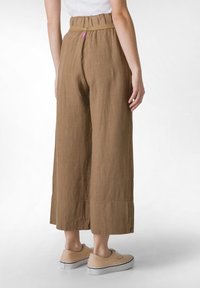 Bruna, vida byxor gjorda av texturerad tyg. Har en rynkad midja och en liten rosa etikett. Matchas med beige sneakers.