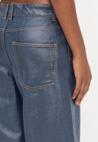 Denim jeans in dark blue, featuring a smooth texture, visible stitching in contrasting orange, and a back pocket with a rectangular shape.