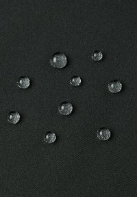 Gocce d'acqua su una superficie di tessuto nero testurizzato, di dimensioni variabili, con superfici chiare e riflettenti che mostrano motivi distinti.