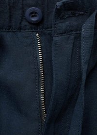 Tessuto blu scuro con una zip e dettagli di chiusura con bottone visibili. Presenta una lavorazione testurizzata e una finitura pulita sui bordi.