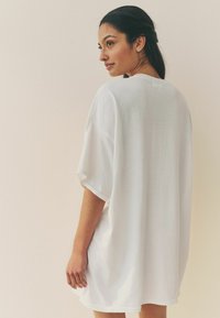 Vit oversized T-shirt gjord av mjukt bomullstyg, med korta ärmar och en enkel, ren design med minimal detaljer.