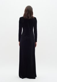Black, long-sleeve velvet gown with a fitted silhouette. The dress extends to the floor, featuring a smooth texture and minimal design details.