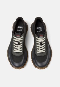 Sneaker impermeabili neri e grigi con chiusura a lacci, tomaia strutturata, marchio Gore-Tex e suole in gomma marrone con battistrada pronunciato.