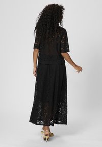 Schwarzes Spitzenkleid mit lockerem Schnitt, kurzen Ärmeln und langem Rock. Der Stoff hat ein florales Muster und eine durchsichtige Textur.