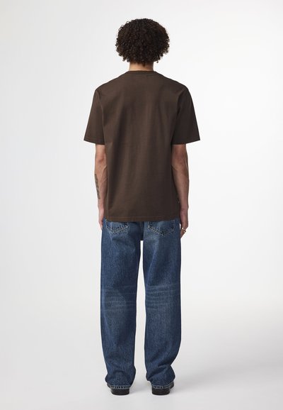 T-shirt in cotone marrone con collo a giro, maniche corte e una vestibilità rilassata, abbinata a jeans in denim blu dal taglio morbido.