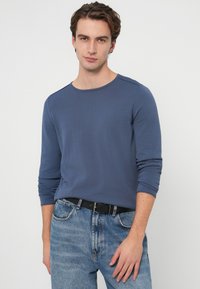 Granatowa koszula z długim rękawem o okrągłym dekolcie i teksturowanej tkaninie, w zestawie z jasnoniebieskimi dżinsami i czarnym paskiem.