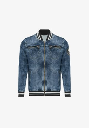 Veste bomber en denim bleu avec col, poignets et ourlet côtelés rayés noir et blanc, fermeture éclair devant, poches poitrine et latérales zippées, et patch sur la manche gauche.