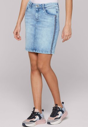 Hellblauer Denimrock mit geradem Schnitt, ausgestattet mit Fronttaschen, einem Reißverschlussdetail an der Seite und gesäumten Kanten. Trägt dazu mehrfarbige Sneakers.