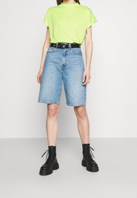 Neonowa zielona koszulka z krótkim rękawem, połączona z jasnoniebieskimi dżinsowymi szortami, czarnym paskiem i masywnymi czarnymi butami na sznurowadła. Prosty design, casualowy wygląd.