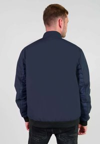 Marineblauwe bomberjack met een gequiltte textuur op de mouwen en een gladde body. Voorzien van een geribbelde tailleband en kraag.