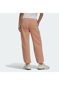 Rosa sweatpants gjorda av mjukt material med avslappnad passform, utrustade med elastisk midja och manchetter vid anklarna, i kombination med vita sportskor.