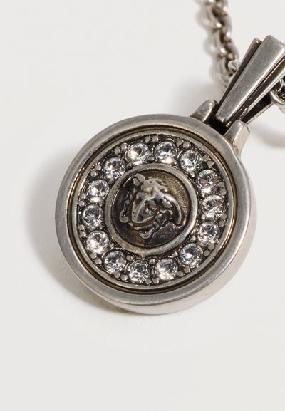 Pendentif rond en argent avec un emblème central de tête de lion entouré d'un cercle de pierres précieuses claires et étincelantes sur une chaîne.