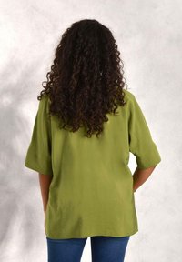 Olive green oversized shirt with short sleeves, smooth texture, straight hem, and relaxed fit paired with blue denim jeans.
