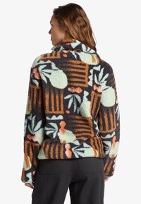 Fleece pullover met een hoge kraag, met een meerkleurig bloemen- en geometrisch patroon op een donkere achtergrond. Zacht, gestructureerd materiaal.