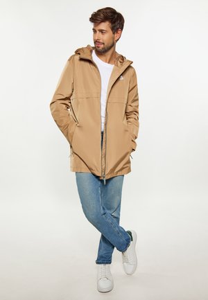 Lys tan vandtæt jakke med hætte og frontlynlås, parret med blå jeans og hvide sneakers, med et rent, minimalistisk design.