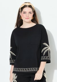Top de algodón negro con mangas three-quarter, adornado con bordados de palmeras beige en las mangas y el dobladillo, y un bolsillo en el pecho.