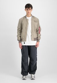 Helebeež bomber jakk sileda tekstuuriga, soonikkätega, haislik tasku varrukal, koos lõdva tumedashalli pükste ja spordijalatsitega.