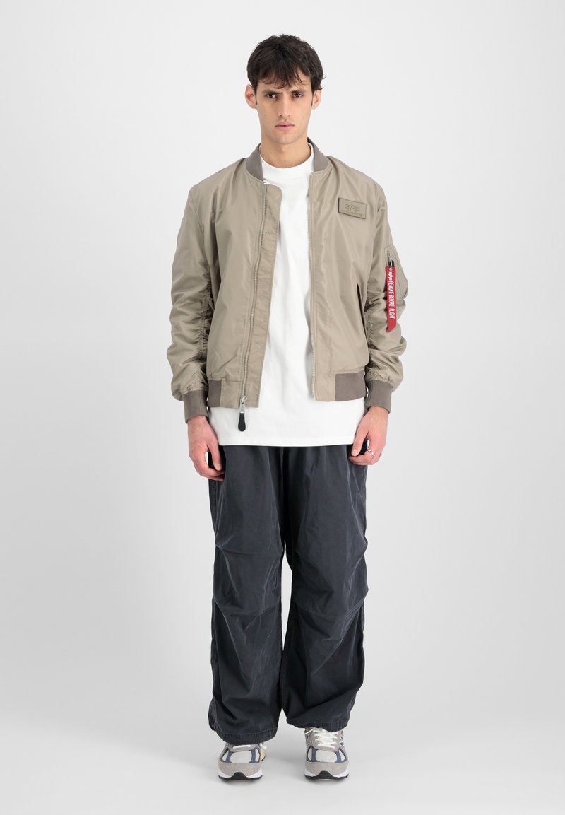 Helebeež bomber jakk sileda tekstuuriga, soonikkätega, haislik tasku varrukal, koos lõdva tumedashalli pükste ja spordijalatsitega.