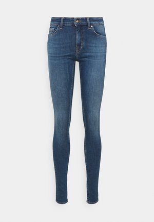 Blauwe skinny-fit spijkerbroek met vijf zakken, knoopsluiting en subtiele vervaging op de dijen tegen een witte achtergrond.