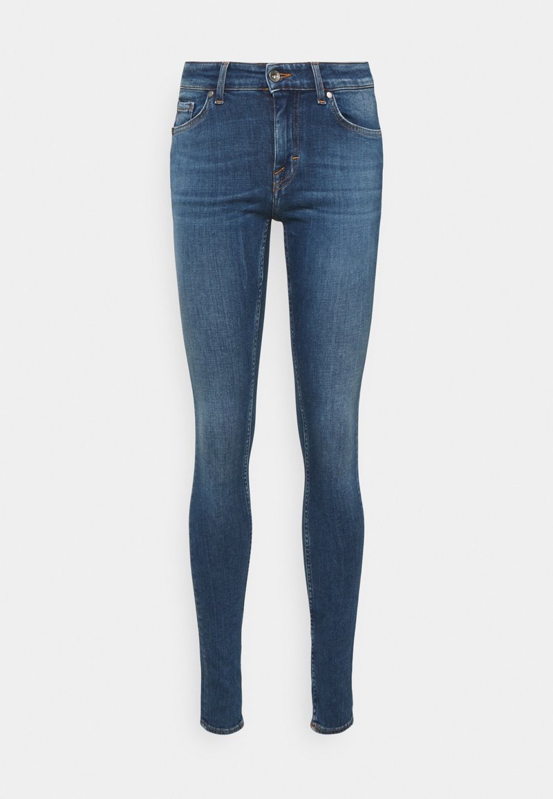 Blauwe skinny-fit spijkerbroek met vijf zakken, knoopsluiting en subtiele vervaging op de dijen tegen een witte achtergrond.