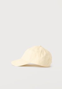 Μπεζ βαμβακερό καπέλο μπέιζμπολ με κυρτή γείσο και ραμμένες τρύπες αερισμού, εμφανιζόμενο από πλάγια σε απλό ανοιχτό φόντο.
