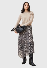 Maglione a maglia beige e gonna maxi fluida in stampa pitone nera e beige. Borsa nera con manico. Stivali neri con tacco in texture liscia.
