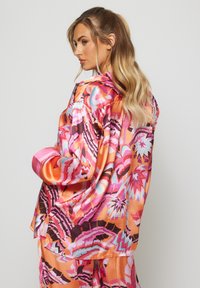 Camisa de satén de manga larga y vibrante, con patrones abstractos multicolores. Incluye un cuello y puños de acento rosa. Corte holgado, textura suave.