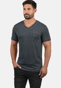 Dunkelgraues, kurzärmliges V-Ausschnitt-T-Shirt aus weichem Material, mit einer Brusttasche auf der linken Seite und einem lässigen Schnitt. Minimalistisches Design.