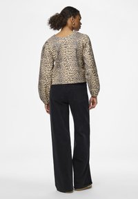 Top de mangas longas, em padrão de pele de leopardo, cortado, nas cores bege e castanho, combinado com calças largas pretas; textura suave com punhos elásticos.