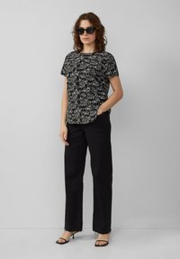 Zwart bloemen t-shirt met korte mouwen, gecombineerd met zwarte wijde broek en zwarte haksandalen, met gestructureerde patronen en een relaxte pasvorm.