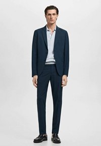 Marineblaues Outfit mit einem maßgeschneiderten Blazer und passenden Hosen, kombiniert mit einem hellblauen Poloshirt. Der Look wird mit schwarzen Schuhen abgerundet.