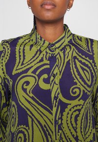 Skjorta med krage i paisleymönster i mörkgrön och marinblå. Tillverkad av ett mjukt tyg med blå knappar som går ned längs framsidan.