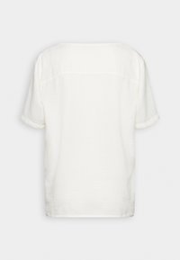 Bílá krátká košile s volným střihem, texturovaná látka a rovný lem. Šev detail na zádech, bez viditelných vzorů nebo akcentů.