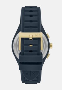 Morsko plava silikonska sat sa kopčom od nehrđajućeg čelika u zlatnoj boji. Ima teksturirani remen i minimalistički dizajn. Stražnja strana je prozirna.