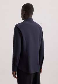 Camicia a maniche lunghe blu scuro con colletto a punta, realizzata in tessuto liscio. Presenta un orlo curvo e polsini con bottoni, caratterizzandosi per un design minimalista.