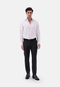 Camicia rosa chiaro con colletto all'inglese, taschino a sinistra, abbinata a pantaloni neri eleganti e scarpe double monk strap nere.