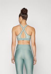 Sujeción deportiva en verde claro con un diseño de tirantes cruzados. Presenta una tela de malla con un patrón y una banda ancha con branding. Leggings a juego de cintura alta.