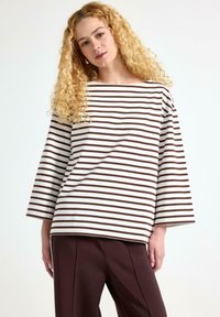 Stribet langærmet top i hvid og brun, med en bred halsudskæring og afslappet pasform. Stylet med mørkebrune bukser i glat stof.