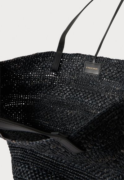Sac fourre-tout tissé noir avec des fines bretelles noires et une petite étiquette rectangulaire portant la mention "By Malene Birger" à l’intérieur.