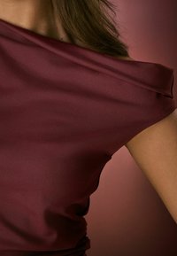 Burgunderfarvet off-the-shoulder top lavet af glat stof; har et draperet design med subtil glans og en tætsiddende silhuet.