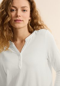 Bílý dlouhý rukáv henley top s v-výstřihem a tříknoflíkovým zapínáním, vyrobený z měkké tkaniny, s pohodlným střihem a jemným leskem.